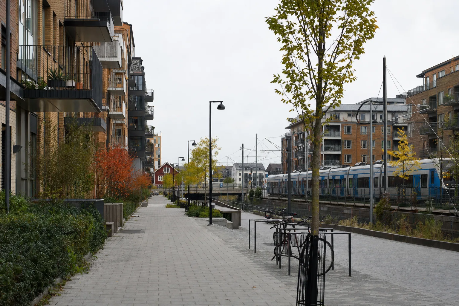 Bostadskvarter med gångstråk, cykelställ och pendeltåg i bakgrunden under dagsljus.